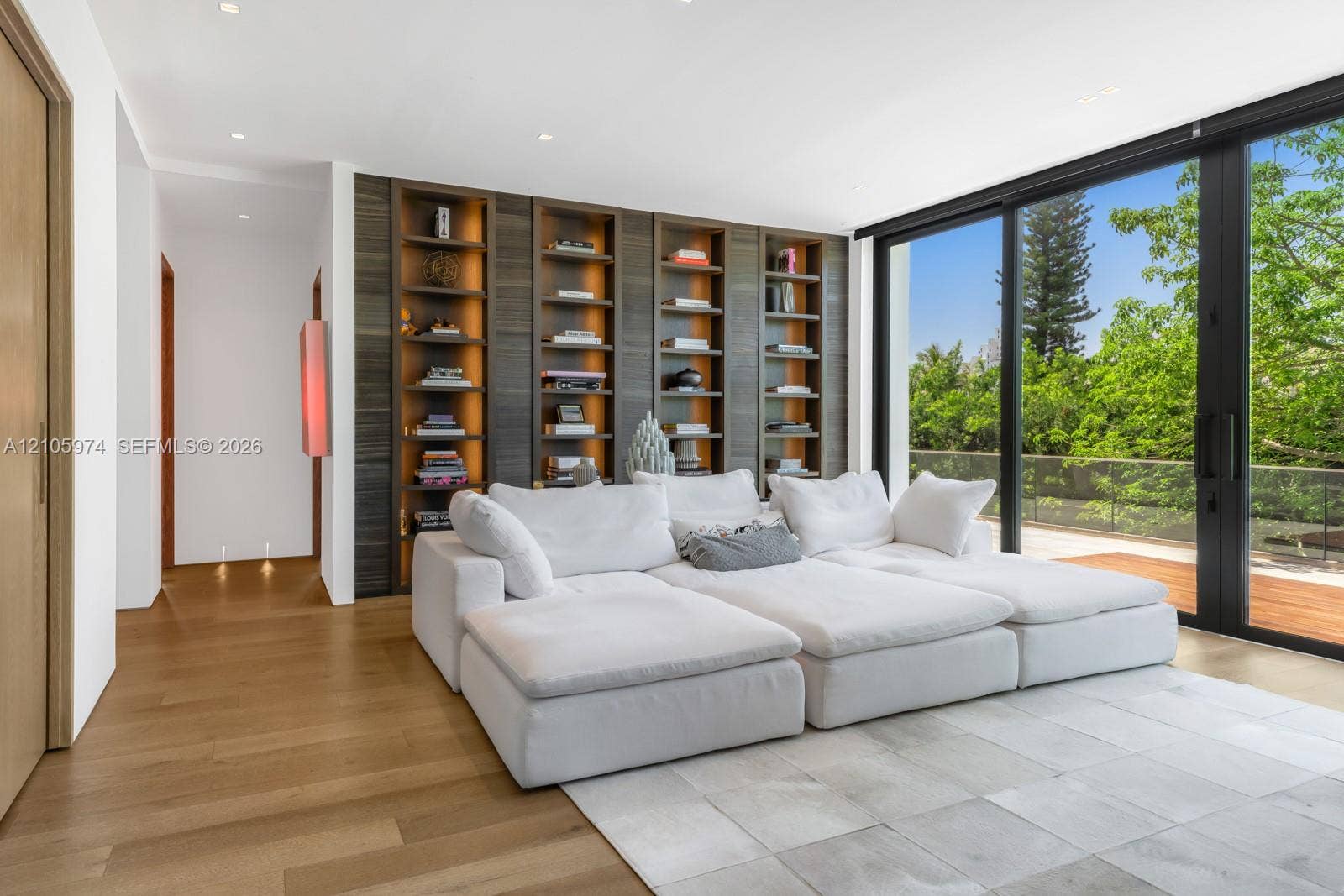 4395 Pine Tree Drive, Miami Beach, FL 33140 Custom floor-to-ceiling built-in shelving with integrated warm lighting, wide-plank wood-finish flooring, and expansive floor-to-ceiling sliding glass doors opening to a deck