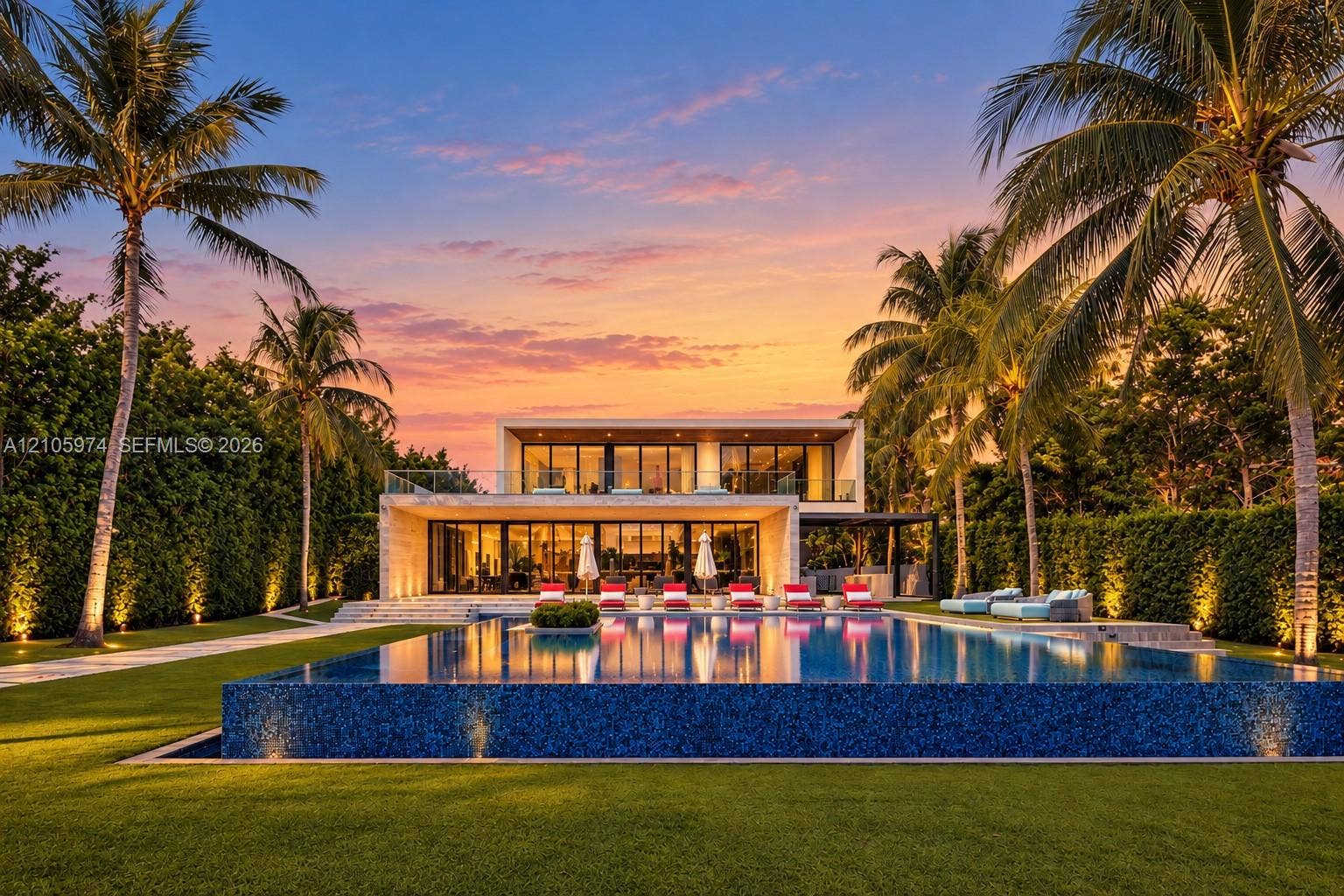 4395 Pine Tree Drive, Miami Beach, FL 33140 Contemporary two-story residence featuring an expansive infinity-edge pool, tiled patio, glass balcony railing, and manicured landscaping