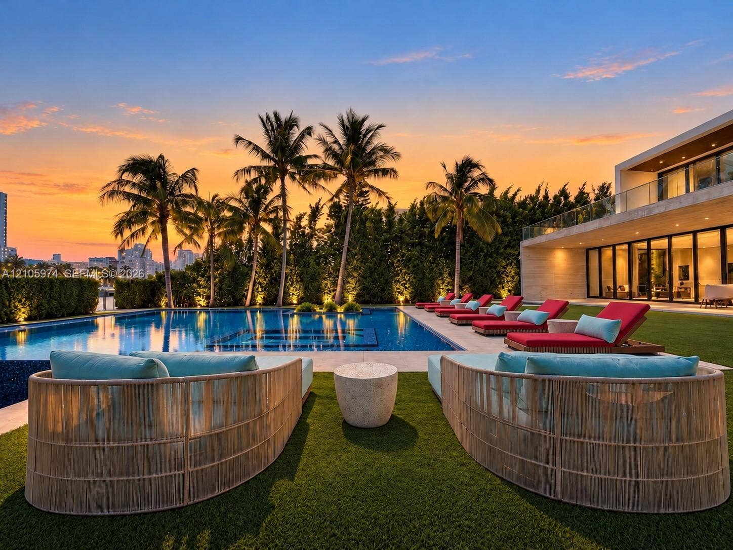 4395 Pine Tree Drive, Miami Beach, FL 33140 Outdoor living space featuring an inground swimming pool with stone tiling, synthetic grass lawn, perimeter hedges, and a glass-railed second-level balcony