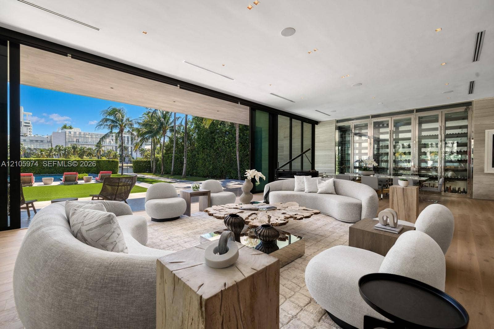 4395 Pine Tree Drive, Miami Beach, FL 33140 Floor-to-ceiling glass retractable wall, wide-plank wood-finish flooring, custom glass-enclosed wine storage, recessed lighting, and expansive stone wall cladding