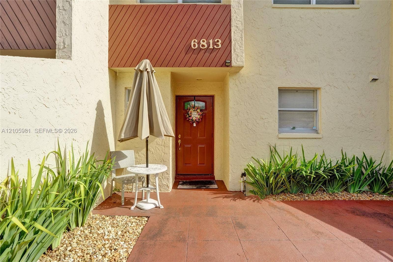 6813 NW 29th Avenue, Fort Lauderdale, Fort Lauderdale, FL 33309 Textured stucco exterior featuring painted wood-panel accenting, a solid door with a glass inlay, and landscaped borders with stone mulch