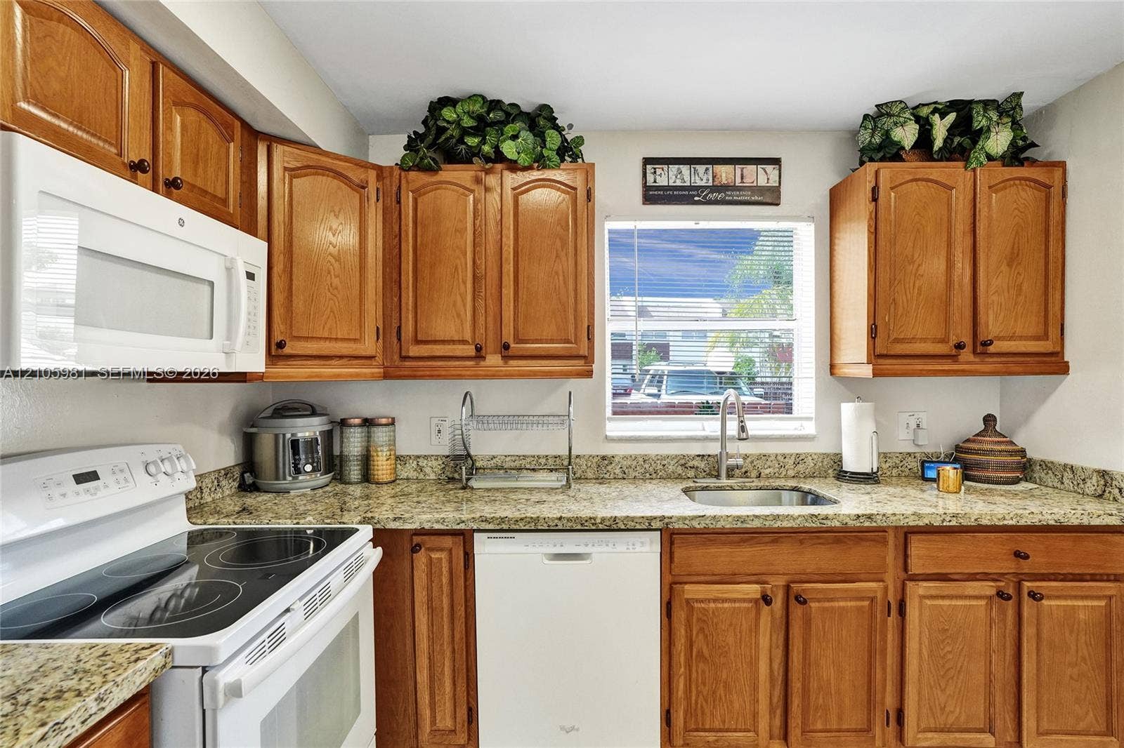 6813 NW 29th Avenue, Fort Lauderdale, Fort Lauderdale, FL 33309 Kitchen featuring warm-toned wood cabinetry, speckled stone-finish countertops, an undermount stainless steel sink with a high-arch faucet, a white built-in microwave, and a white electric range