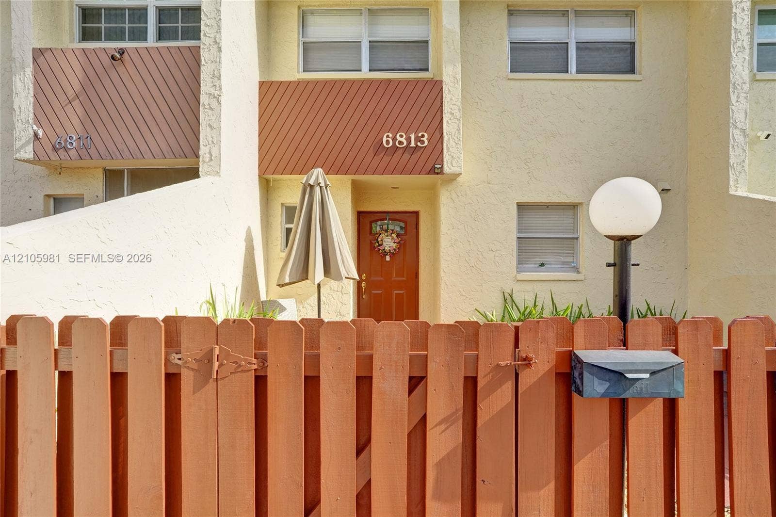 6813 NW 29th Avenue, Fort Lauderdale, Fort Lauderdale, FL 33309 Stucco exterior featuring diagonal wood paneling, multi-pane windows, and a wood-slat privacy fence with an attached mailbox
