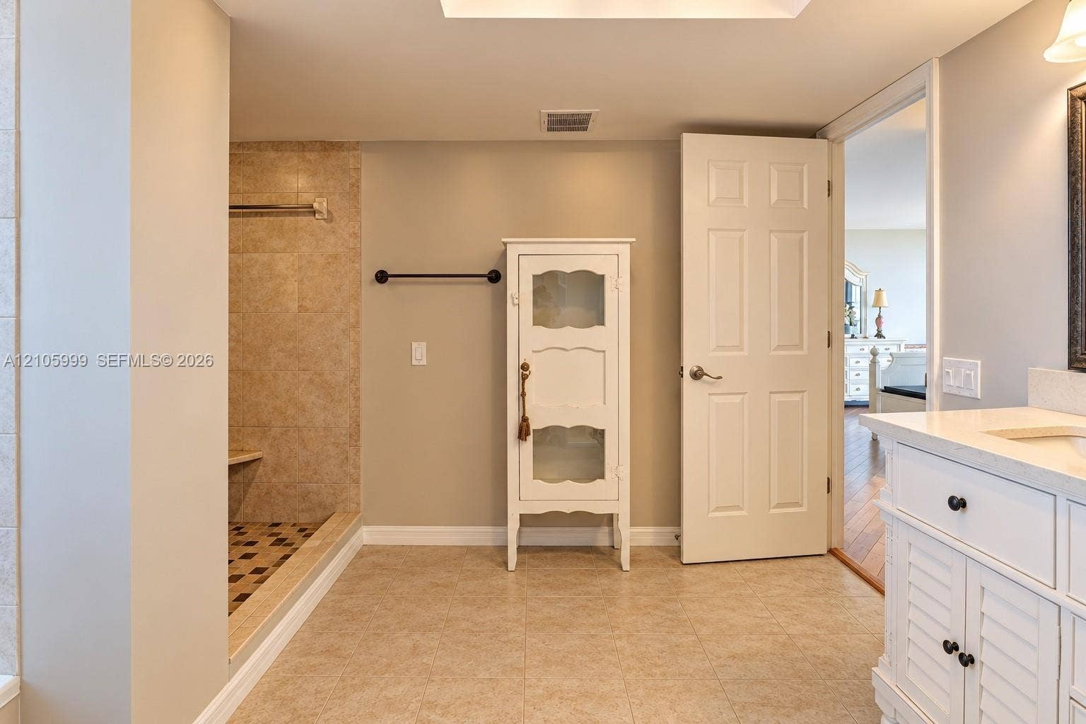 Bathroom featuring a walk-in shower with tiled surround, built-in vanity with countertop sink, and neutral tile flooring
