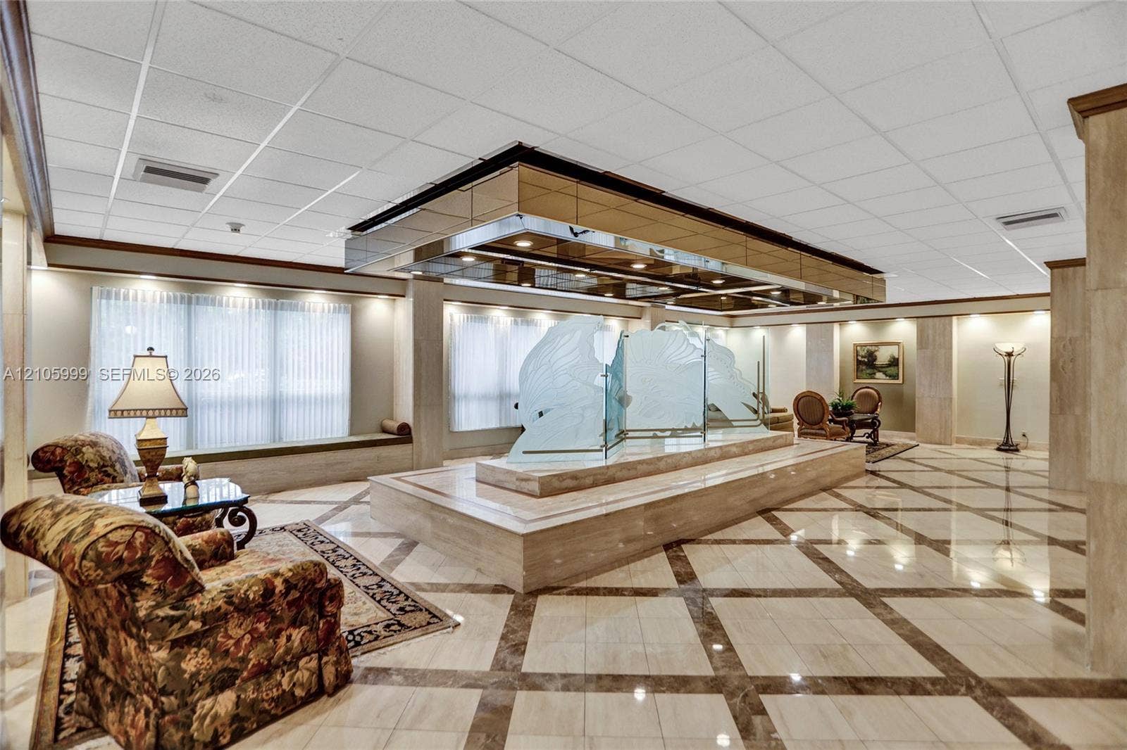 Grand lobby featuring stone-tile flooring in a geometric pattern, custom etched-glass sculptural centerpiece, elevated stone platform, and recessed tray ceiling with metallic accents