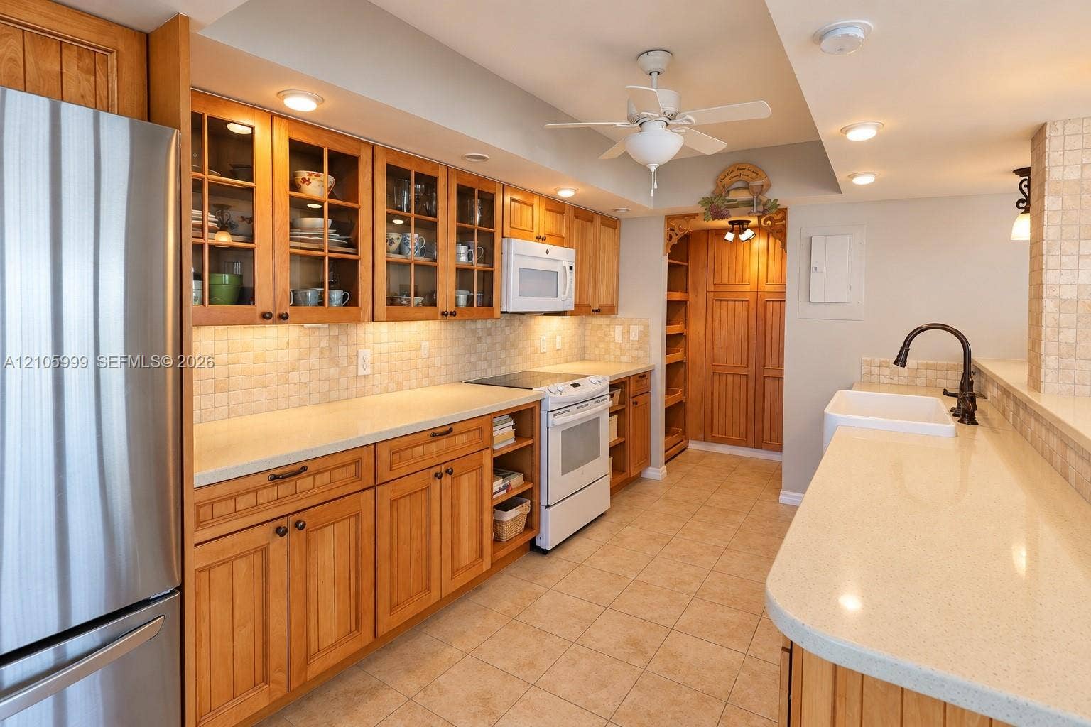 Kitchen featuring custom wood cabinetry with glass-front uppers, solid surface countertops, a tiled backsplash, and a farmhouse-style sink