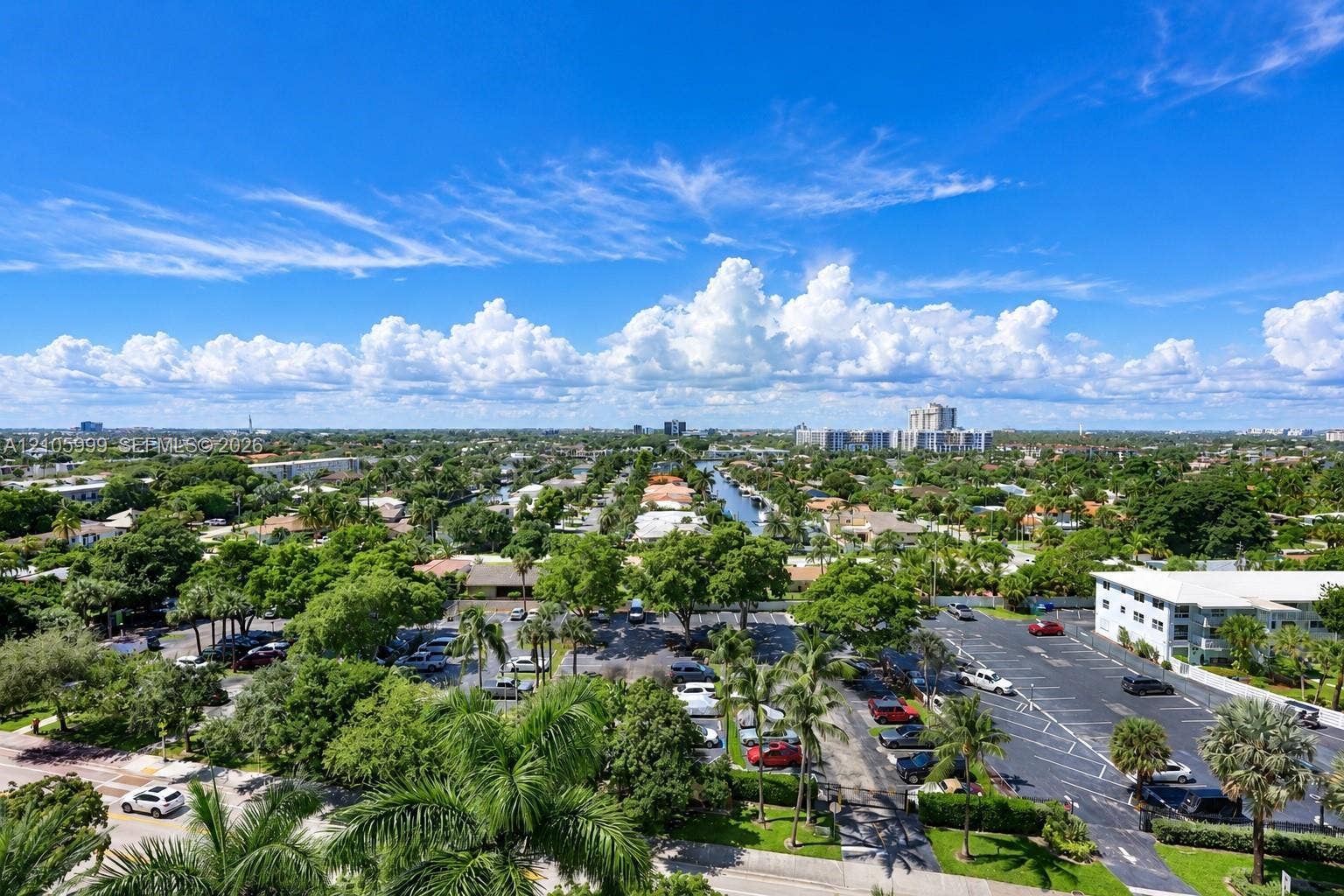 Aerial perspective featuring paved parking areas, mature palm trees, established landscaping, and a central waterway