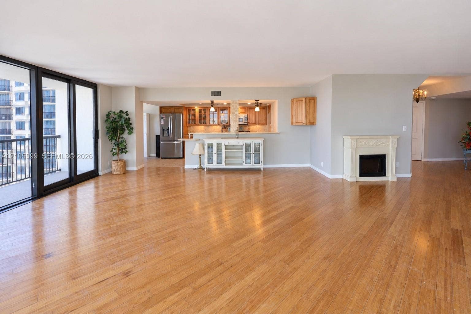 Open-concept interior featuring wood-finish flooring, floor-to-ceiling sliding glass doors, a kitchen pass-through with stone-topped breakfast bar, and a fireplace with a decorative mantel