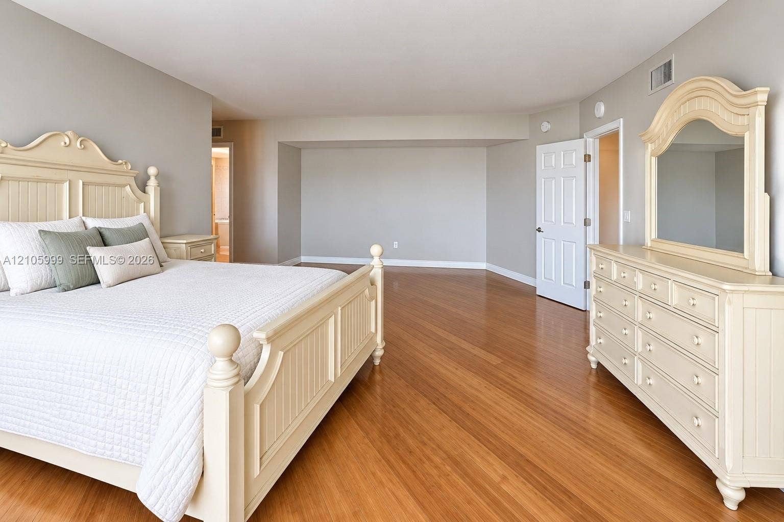 Spacious room featuring wood-finish flooring, neutral wall paint, and a six-panel interior door