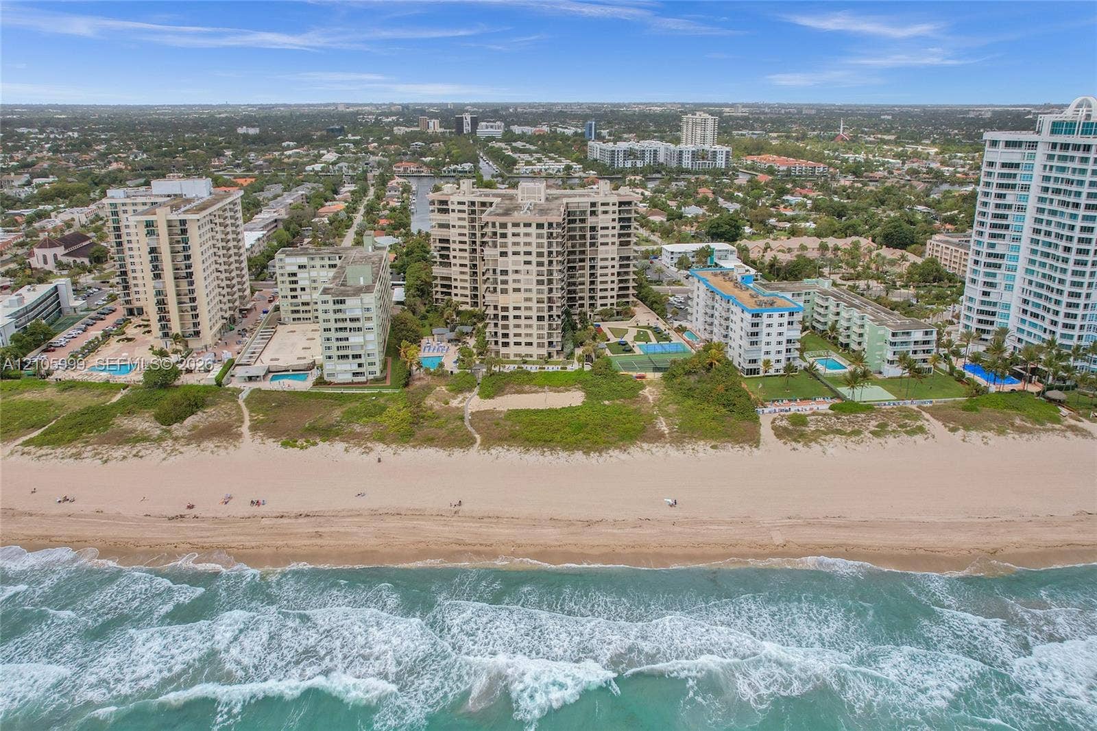 Aerial perspective of high-rise condominium complex featuring direct oceanfront access, private swimming pools, and dedicated hard-surface sports courts