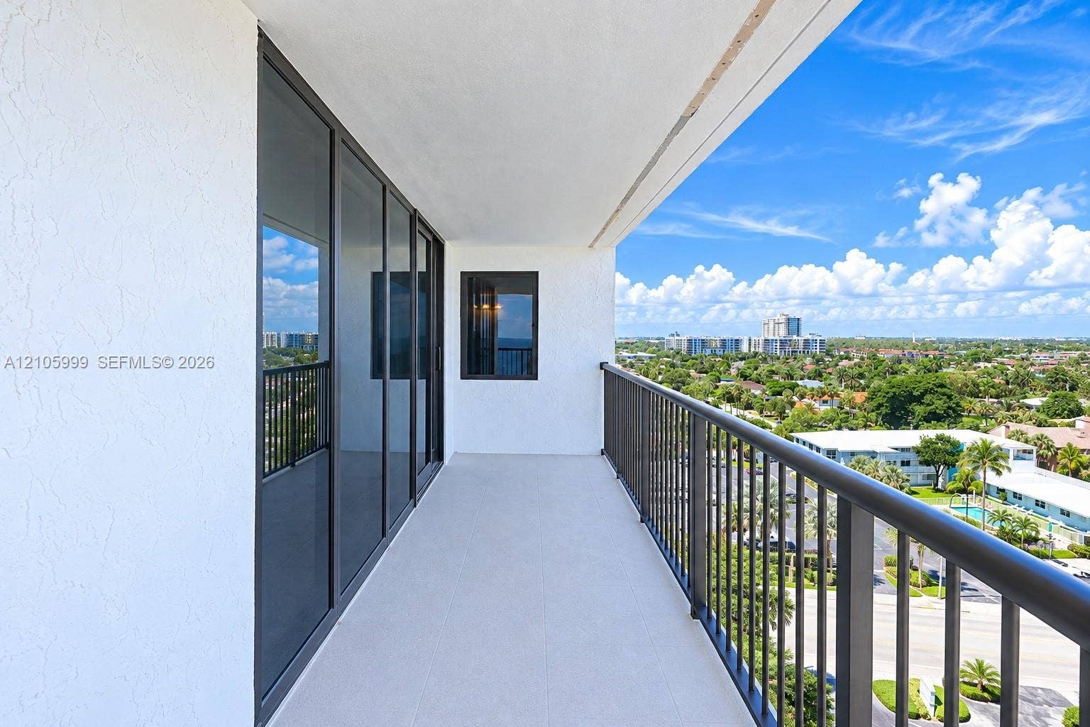 Expansive covered balcony with glass sliding doors, metal railings, and panoramic sightlines overlooking manicured landscaping and the surrounding cityscape