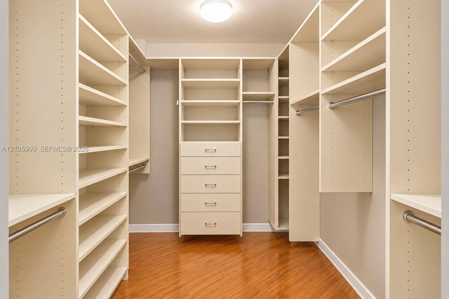 Walk-in closet featuring extensive built-in shelving, integrated five-drawer dresser, metal garment rods, and wood-finish flooring
