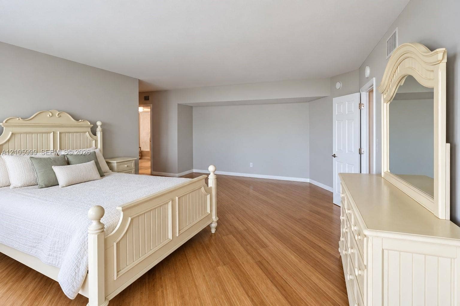 Spacious room featuring wood-finish flooring, neutral wall paint, and a multi-panel door