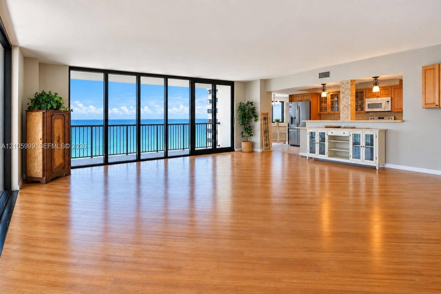 Open-concept interior featuring wood-finish flooring, floor-to-ceiling glass sliding doors, ocean horizon backdrop, and built-in cabinetry with stone-finish surfaces