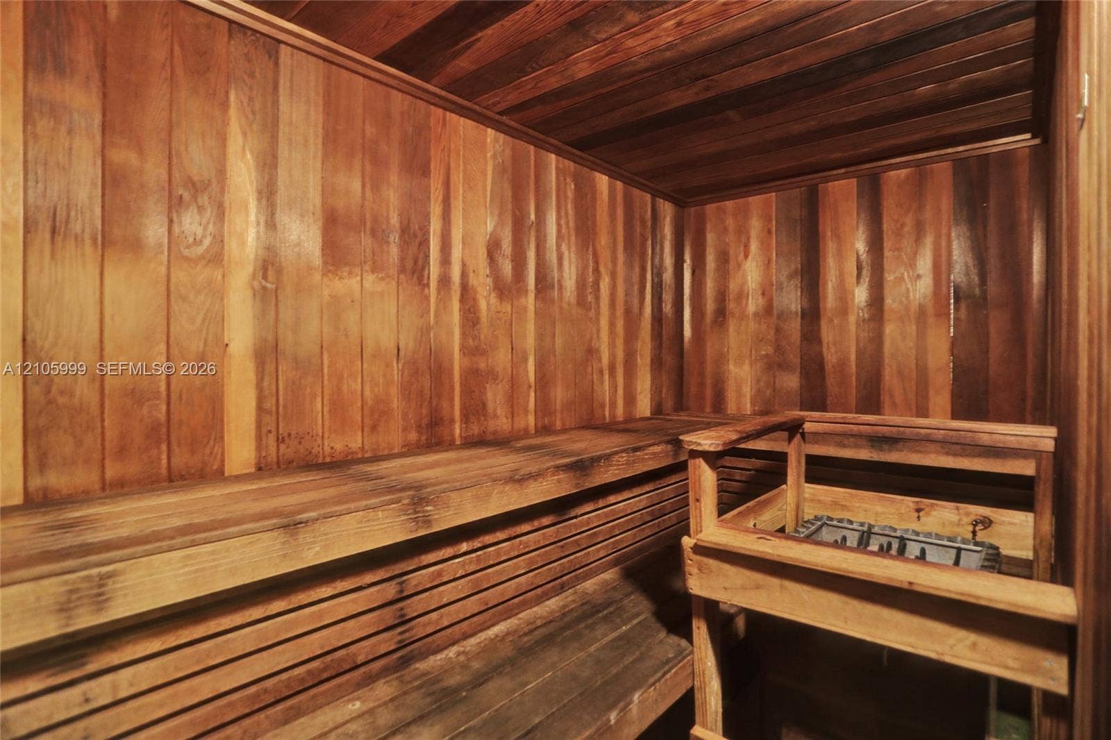 Sauna featuring natural wood-paneled walls and ceiling, integrated multi-tier wood bench seating, and a dedicated heating unit with protective enclosure