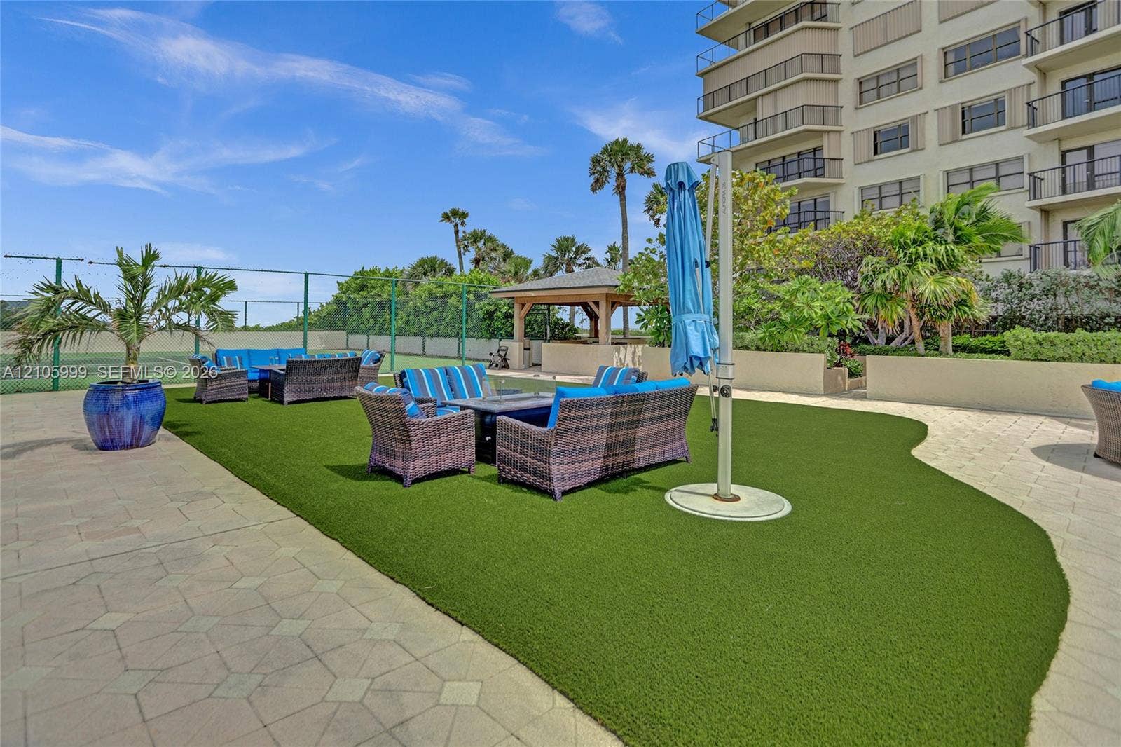 Outdoor recreational area featuring a manicured turf lawn, paved patio, perimeter fencing, and a covered pavilion