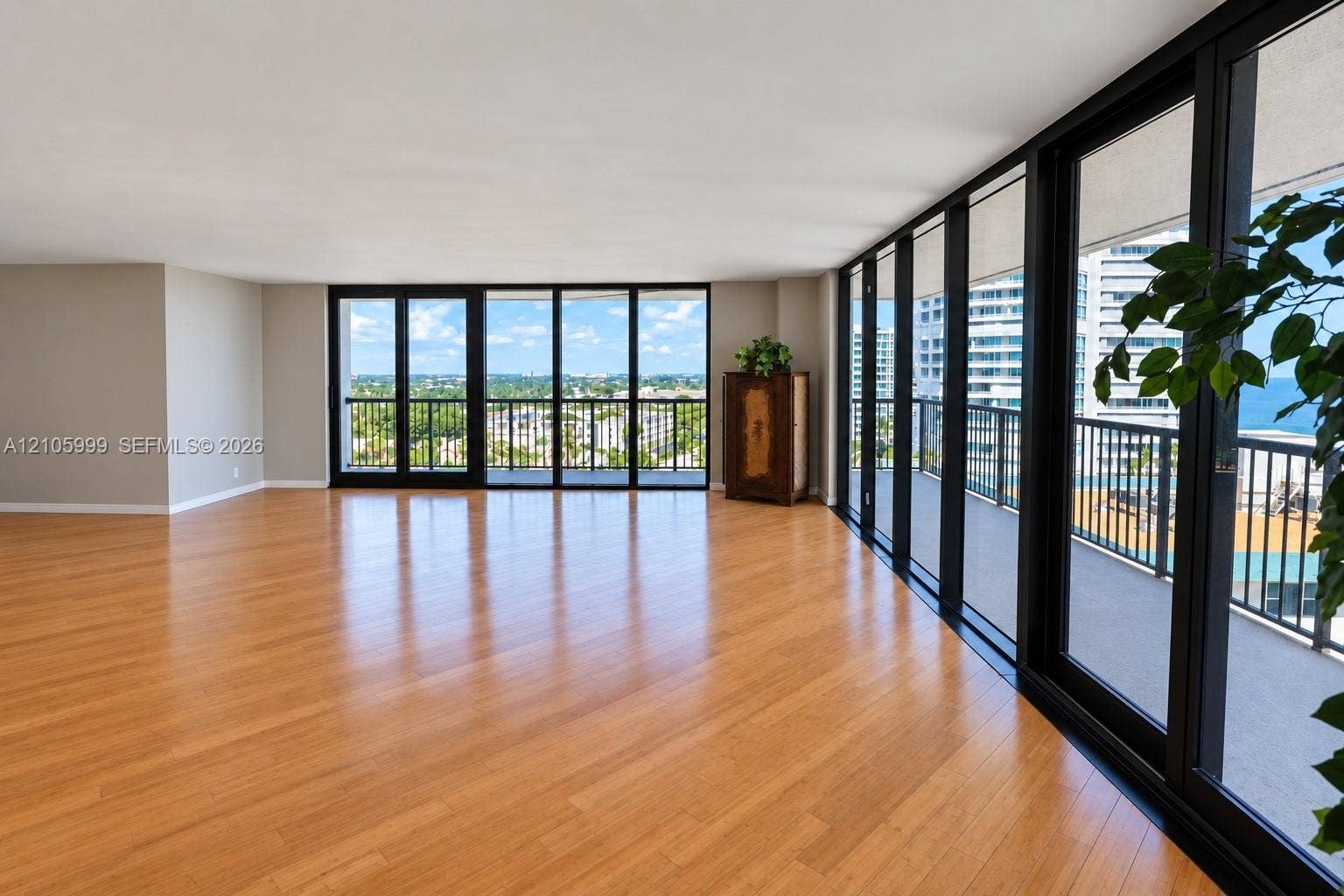 Open-concept interior featuring wood-finish flooring, extensive floor-to-ceiling windows, and access to a wrap-around balcony with metal railings
