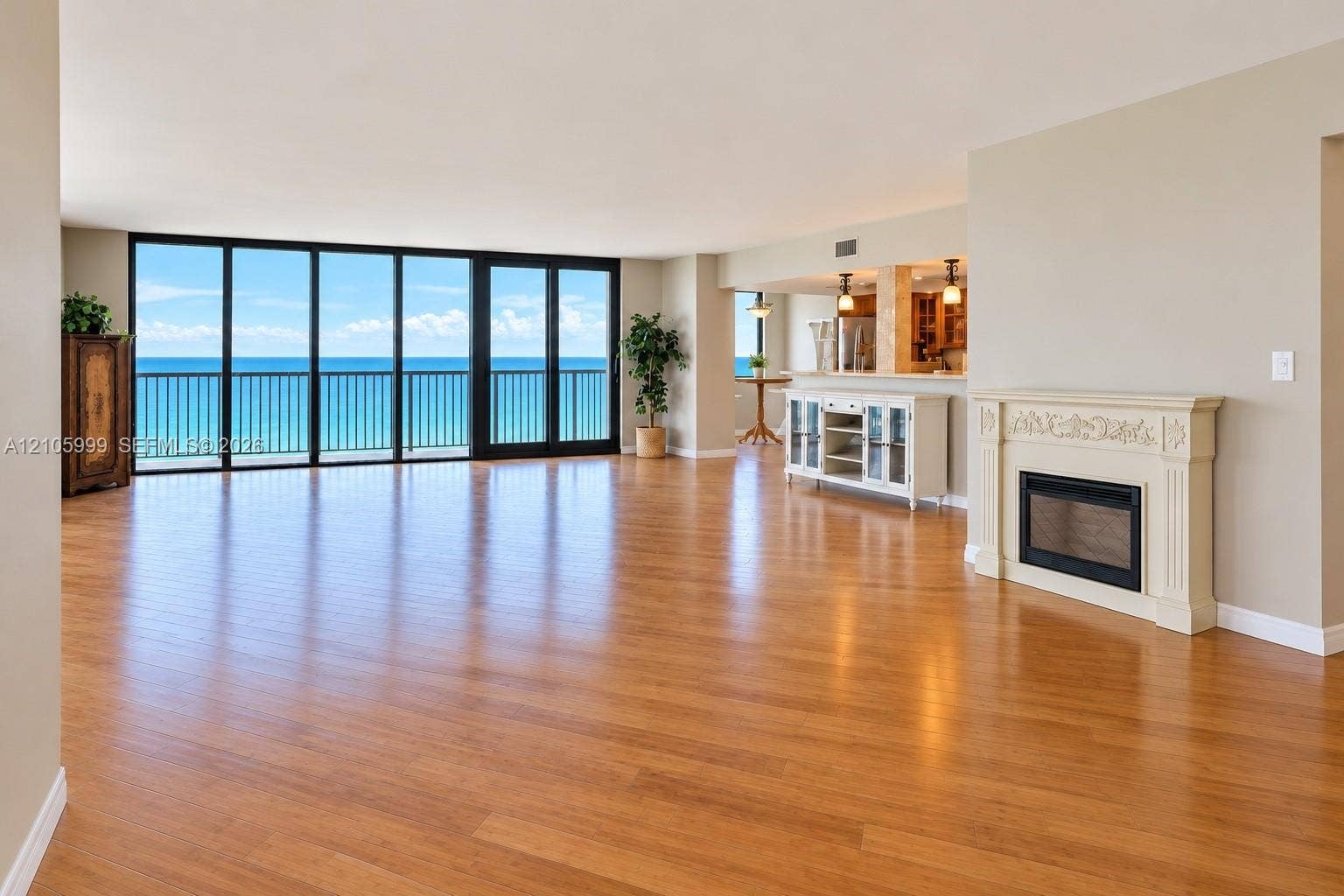 Open-concept living space featuring wood-finish flooring, floor-to-ceiling glass wall, decorative fireplace mantel, and ocean backdrop