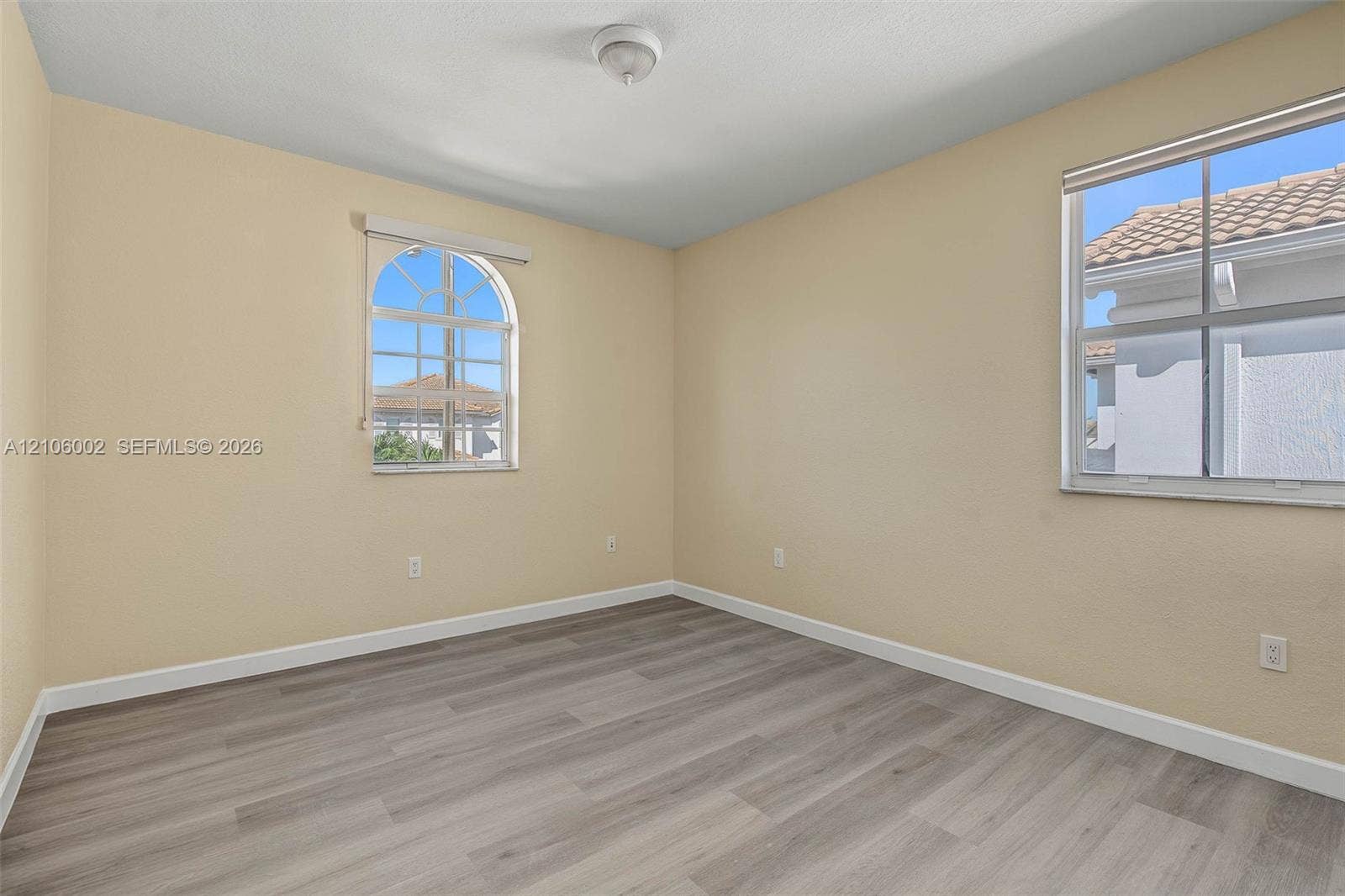 Room featuring wood-finish flooring, an arched window, and a rectangular window with grid muntins