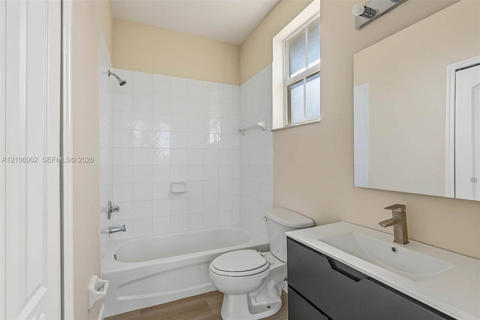 Modern vanity with integrated rectangular sink and metallic faucet, complemented by a white tile tub surround, wood-finish flooring, and a wall-mounted mirror