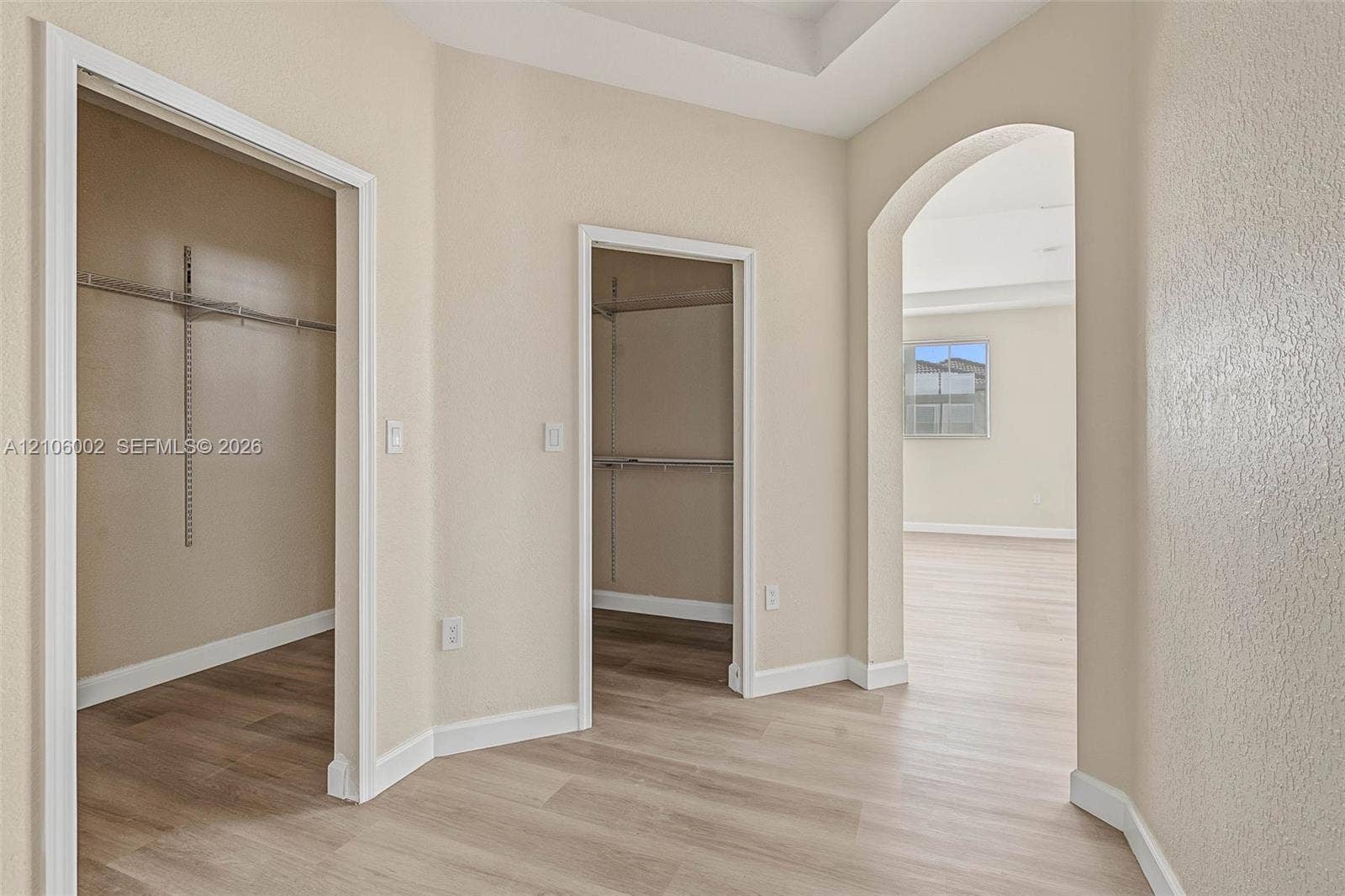 Neutral-toned interior featuring wood-finish flooring, two walk-in closets with built-in shelving, a tray ceiling, and an arched entryway