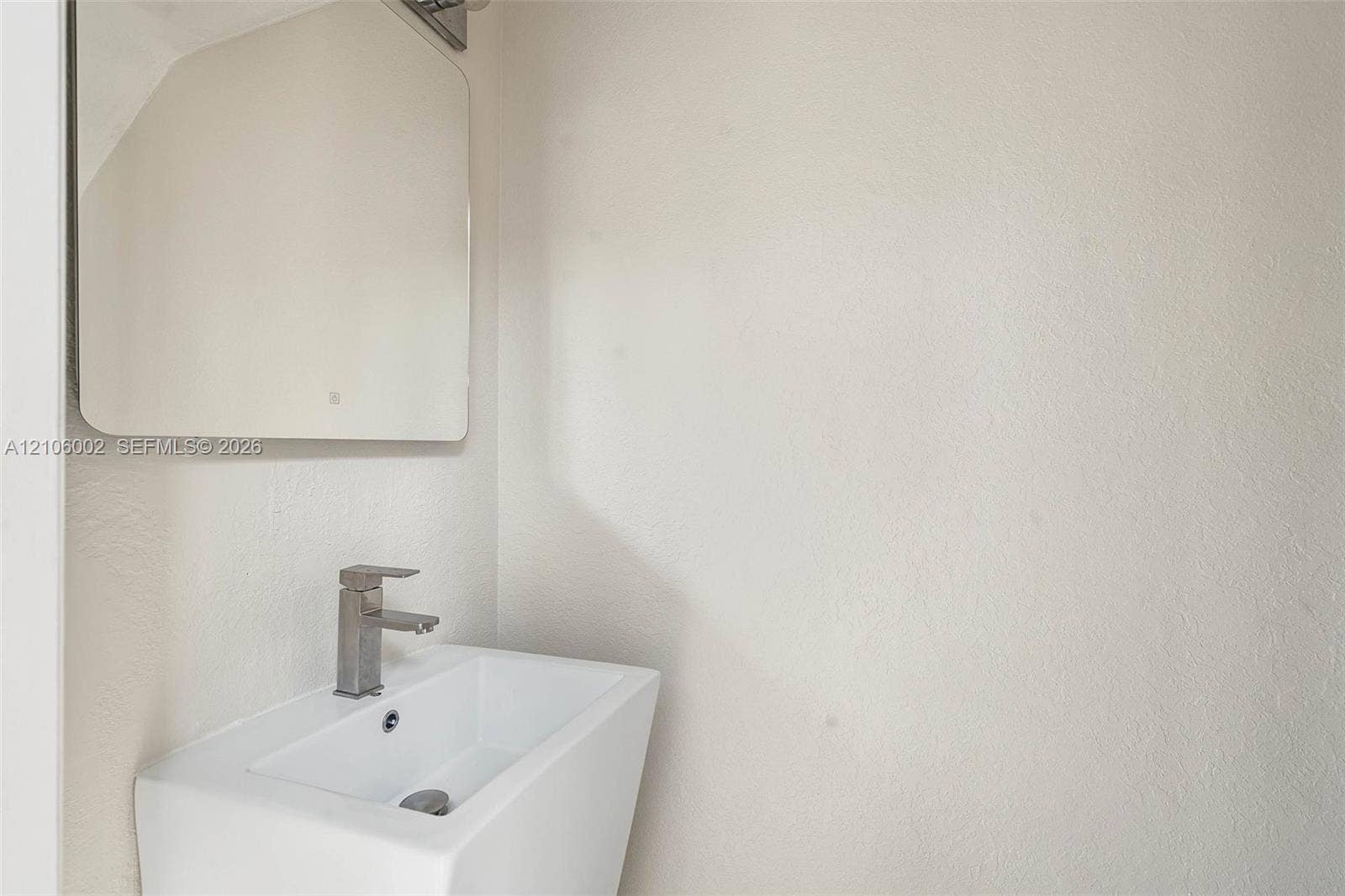 Wall-mounted rectangular basin with a single-handle metallic faucet, complemented by a square-cornered mirror and integrated lighting