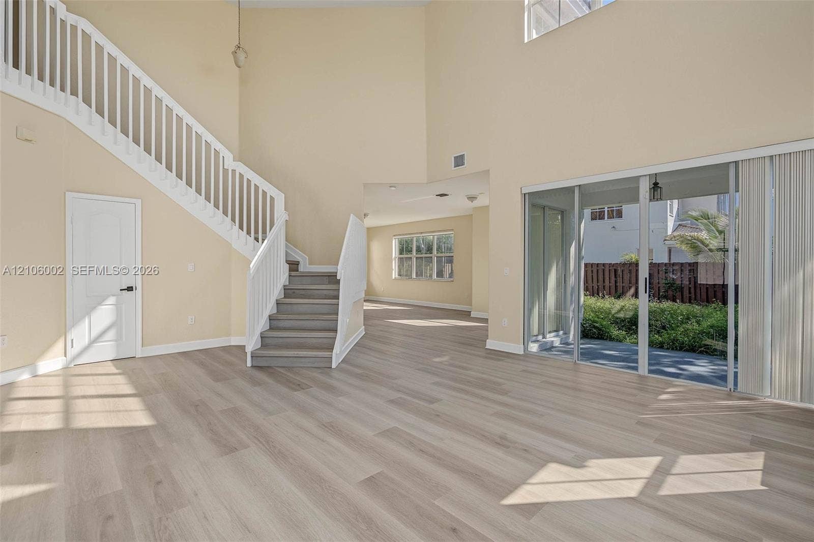 Double-height ceiling, wood-finish flooring, staircase with white railings, and sliding glass doors with exterior patio access