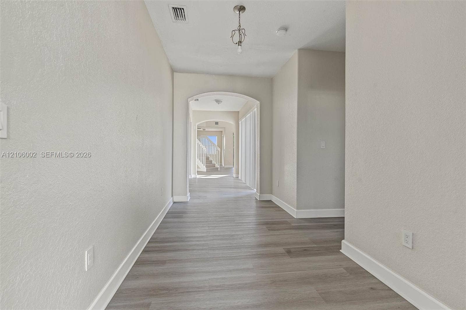 Entryway featuring wood-finish flooring, neutral wall tones, arched architectural detailing, and a hanging pendant light fixture