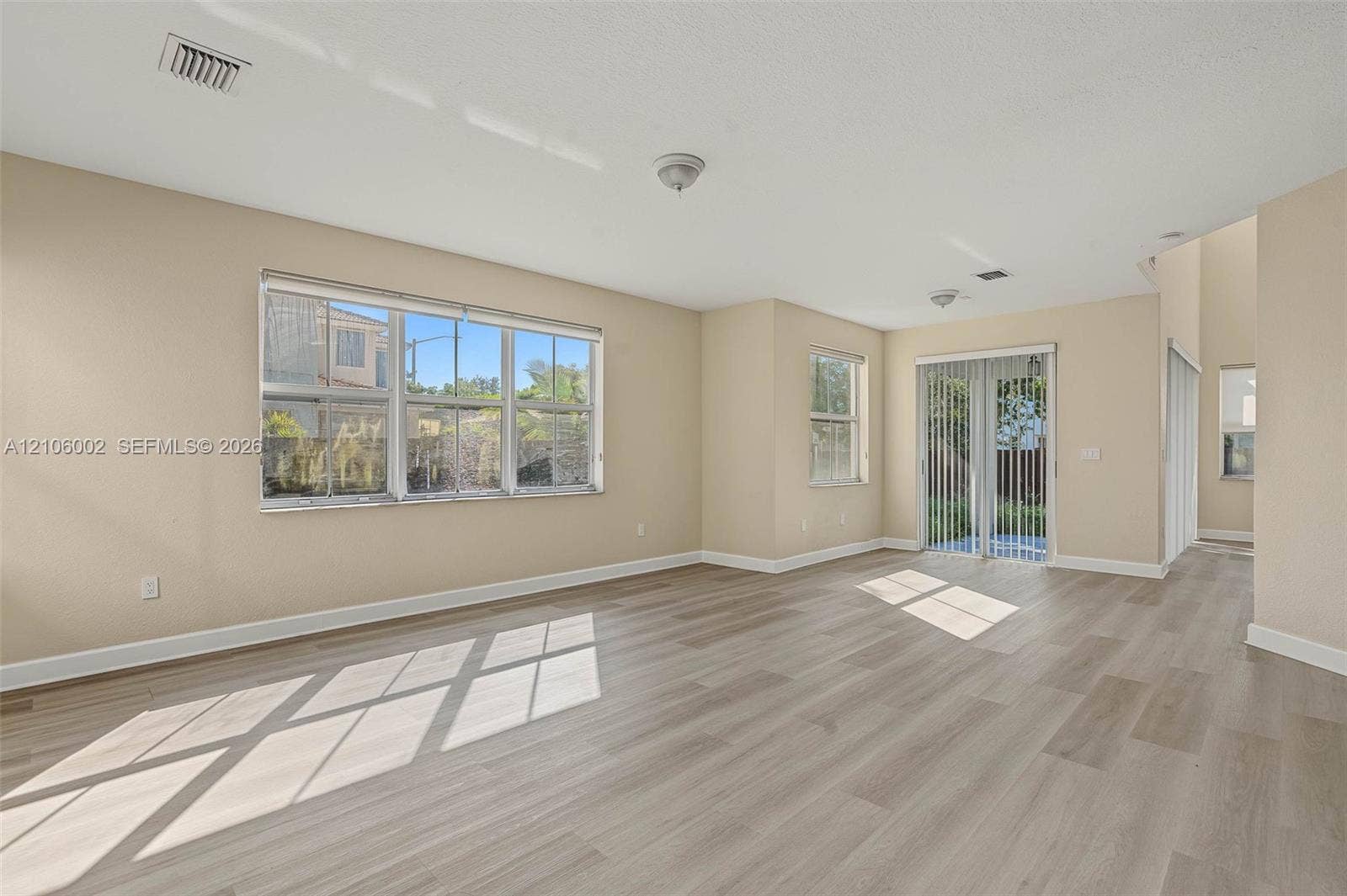 Interior space featuring light-toned wood-finish flooring, large multi-pane windows, and sliding glass patio doors
