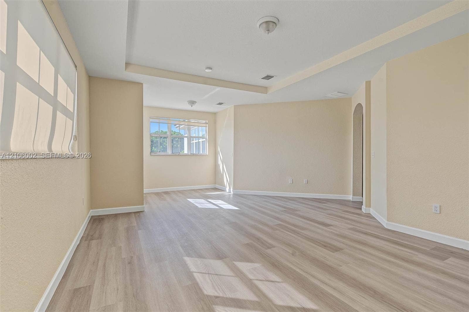 Spacious interior featuring wood-finish flooring, recessed tray ceiling, neutral wall tones, multi-pane windows, and an arched entryway