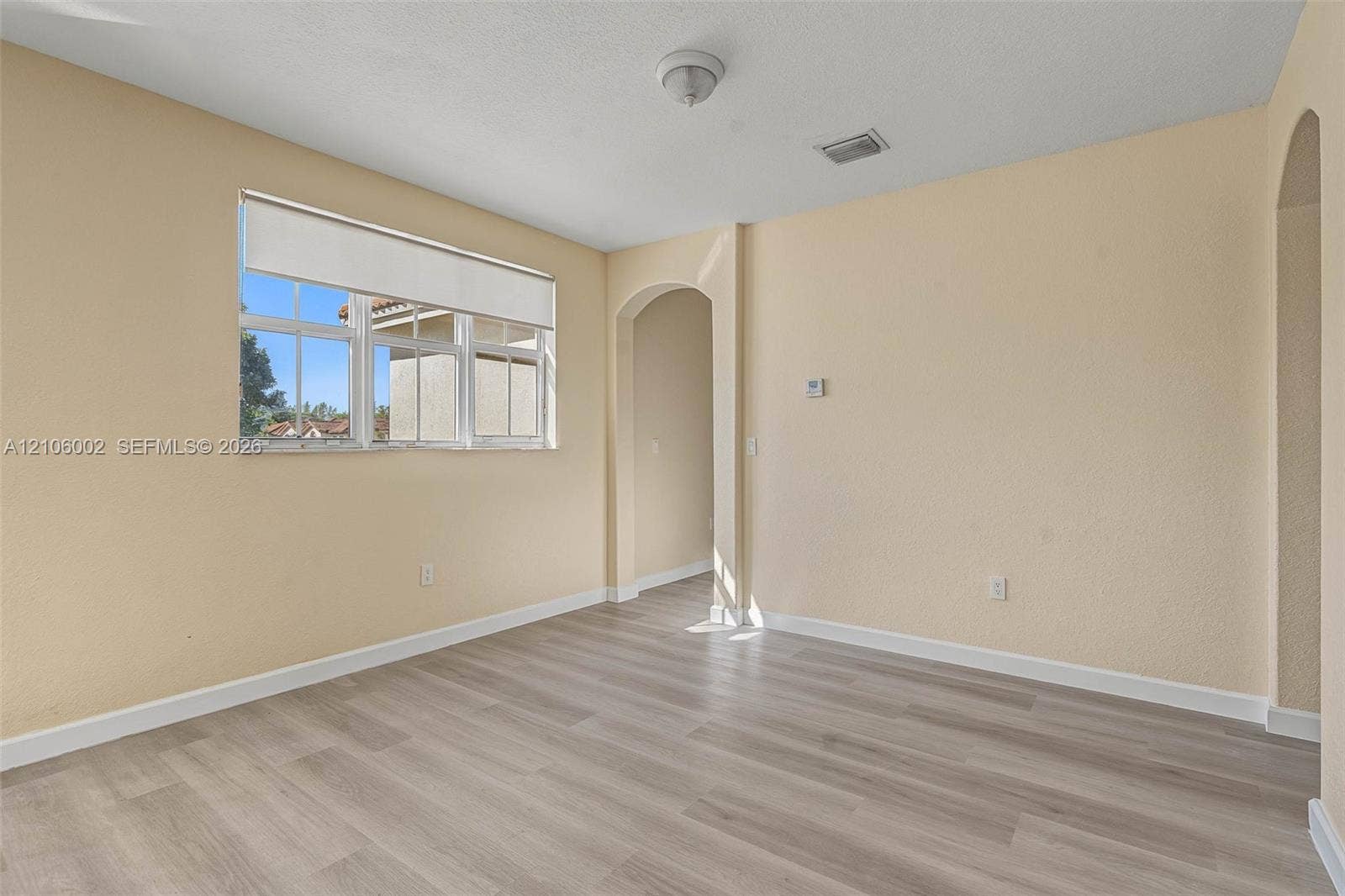 Interior space featuring wood-finish flooring, textured wall finishes, arched entryways, and a multi-pane window with a neutral roller shade