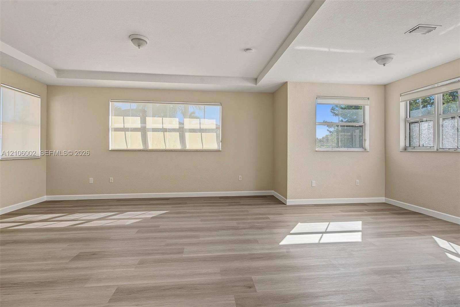 Spacious interior featuring wood-finish flooring, tray ceilings, and multiple windows