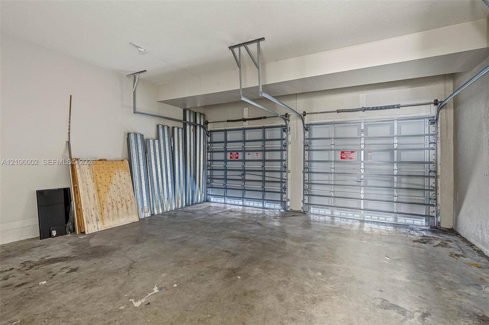 Two-car garage featuring finished concrete flooring, neutral wall paint, and dual metal sectional garage doors with ceiling-mounted operating mechanisms