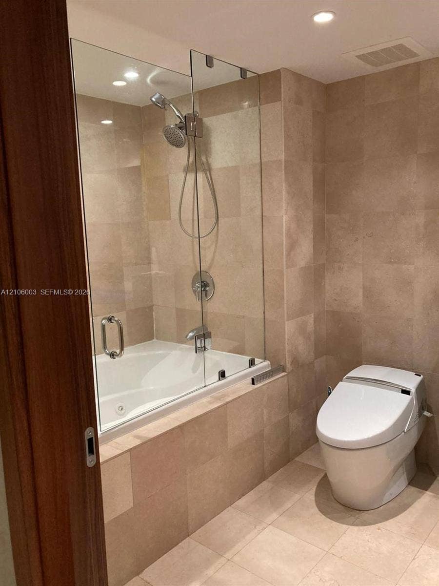 1850 S Ocean Drive, #3309, Hallandale Beach, Hallandale Beach, FL 33009 Bathroom featuring floor-to-ceiling stone-tile surround, soaking tub with a glass panel enclosure, hand-held shower fixture, and a one-piece low-profile toilet