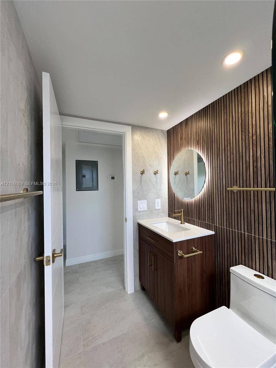 495 Fanshaw L, Boca Raton, FL 33434 Wood-slat accent wall featuring a backlit circular mirror, vanity with a white countertop, and gold-finish hardware throughout
