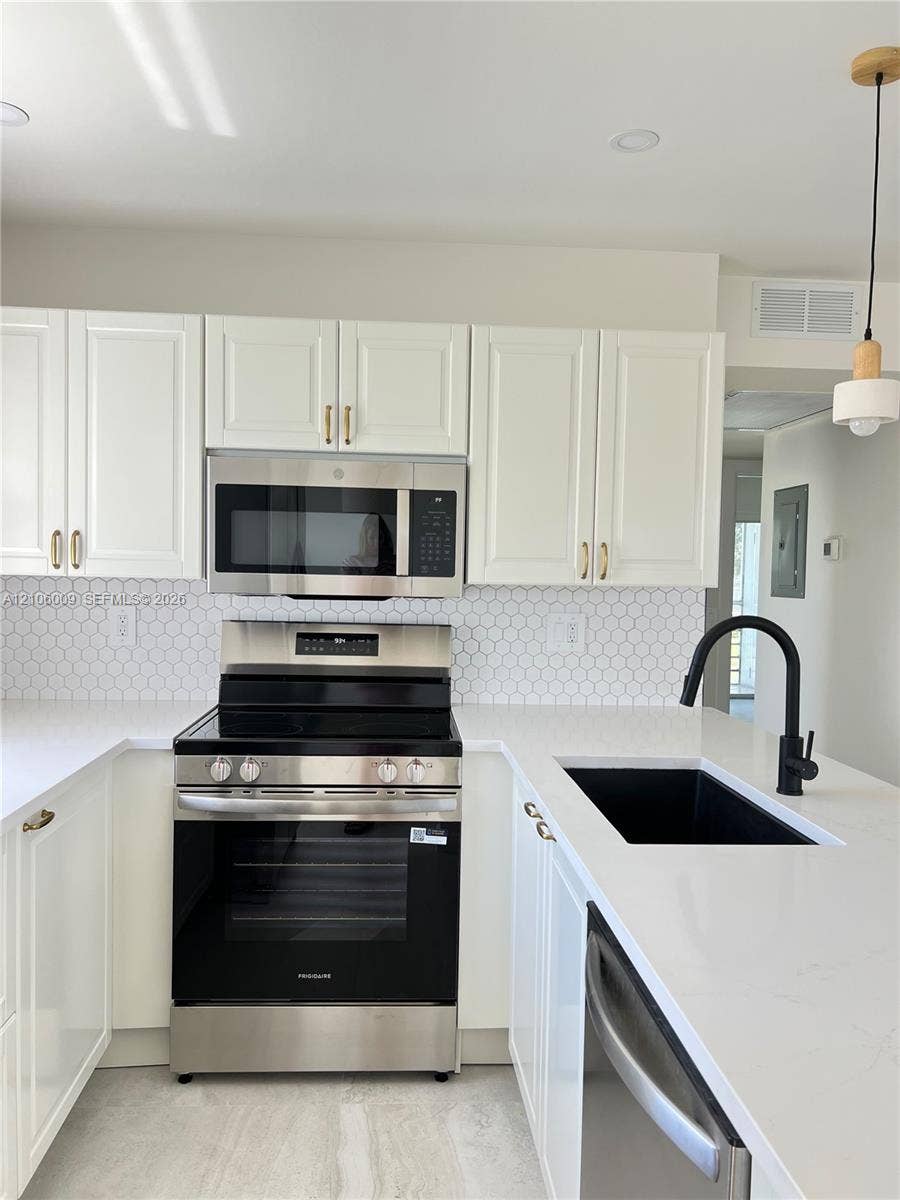 495 Fanshaw L, Boca Raton, FL 33434 White cabinetry with gold-tone hardware, stainless steel appliances, white quartz countertops, white hexagonal tile backsplash, and a black gooseneck faucet