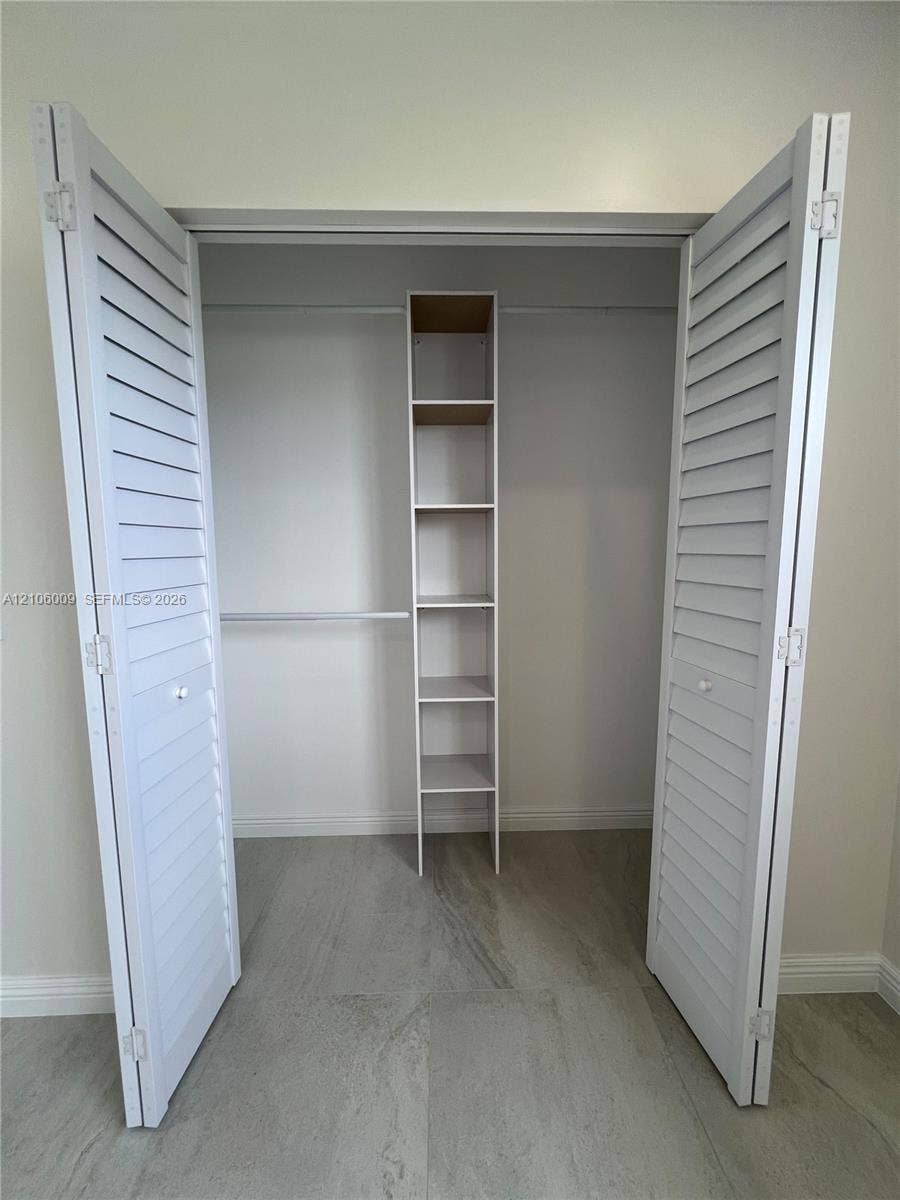 495 Fanshaw L, Boca Raton, FL 33434 Closet featuring white louvered bifold doors, built-in shelving unit, and hanging rod