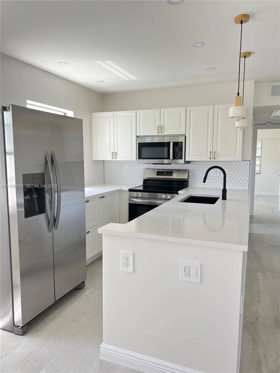 495 Fanshaw L, Boca Raton, FL 33434 Kitchen featuring white shaker-style cabinetry, a quartz countertop, stainless steel appliances, a geometric tile backsplash, and matte black plumbing fixtures