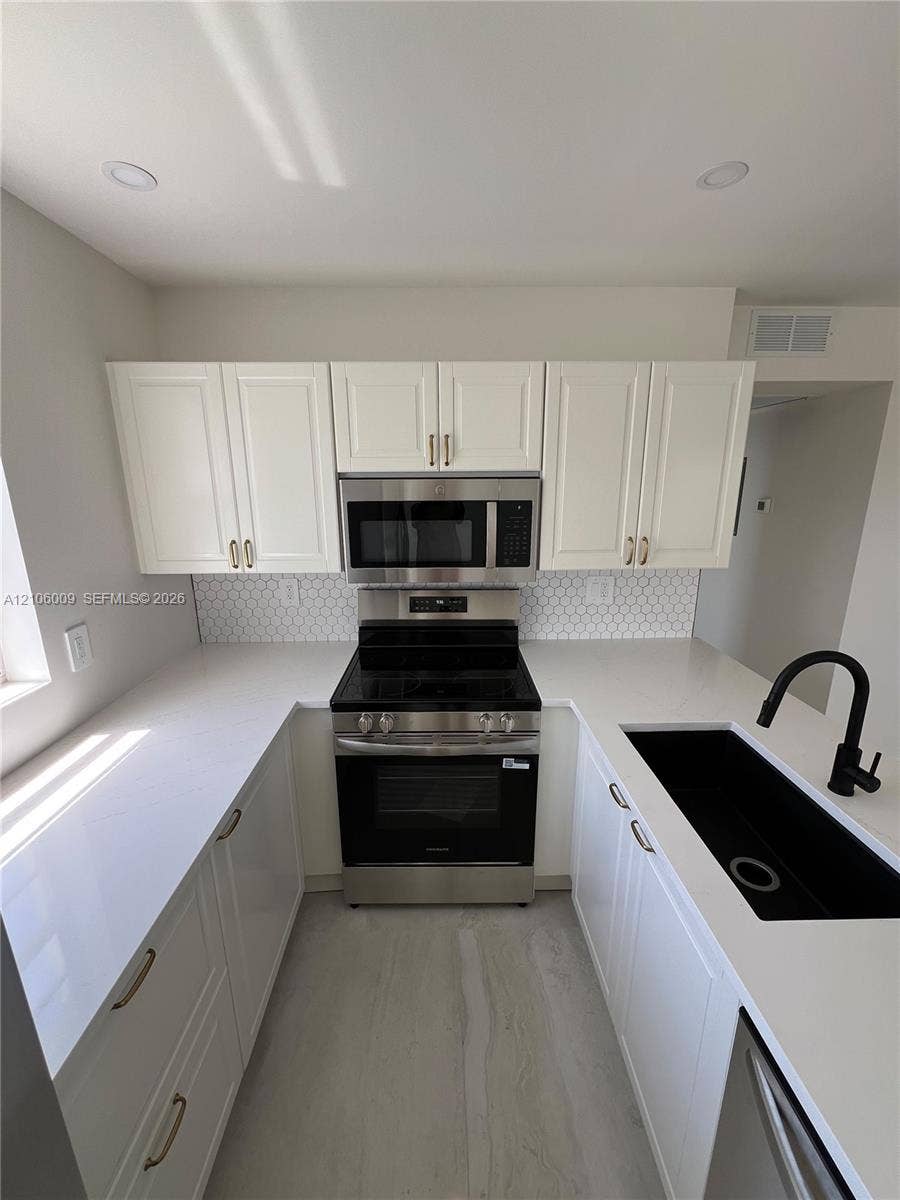 495 Fanshaw L, Boca Raton, FL 33434 Kitchen featuring white cabinetry, quartz countertops, a hexagonal tile backsplash, stainless steel appliances, and a matte black faucet with an integrated undermount sink