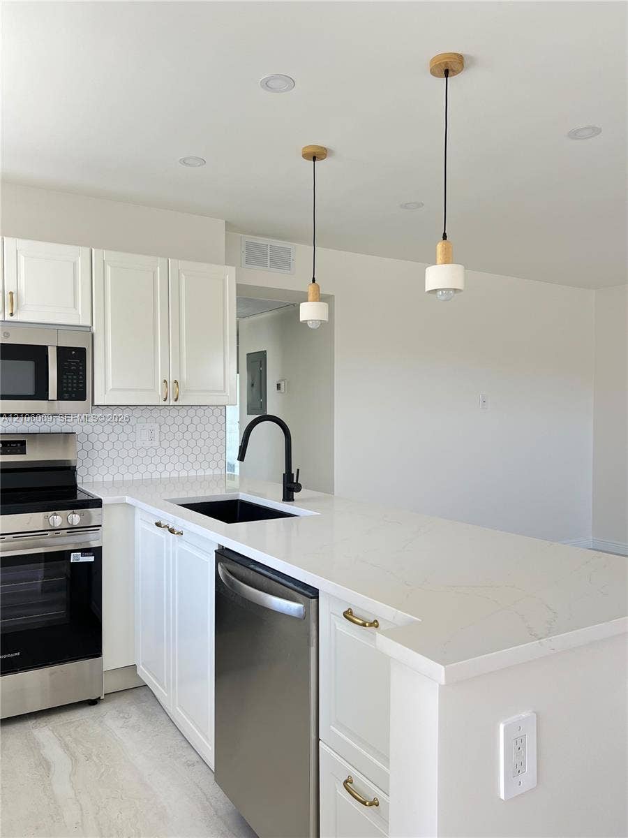 495 Fanshaw L, Boca Raton, FL 33434 Kitchen featuring white cabinetry, quartz countertops, a hexagonal tile backsplash, stainless steel appliances, and matte black plumbing fixtures