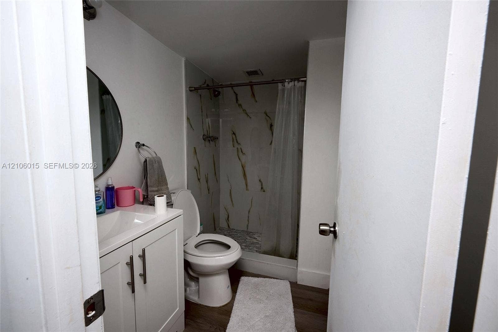 2851 NE 183rd Street, #1109E, Aventura, FL 33160 Bathroom featuring a white vanity cabinet, round wall mirror, and a tub-shower combination with patterned wall tile