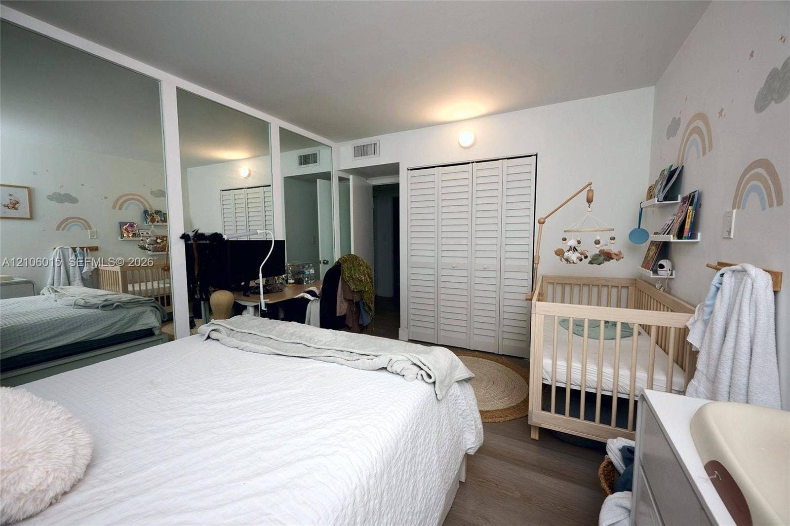 2851 NE 183rd Street, #1109E, Aventura, FL 33160 Bedroom featuring wood-finish flooring, floor-to-ceiling mirrored closet doors, white louvered-style closet doors, and wall-mounted shelving