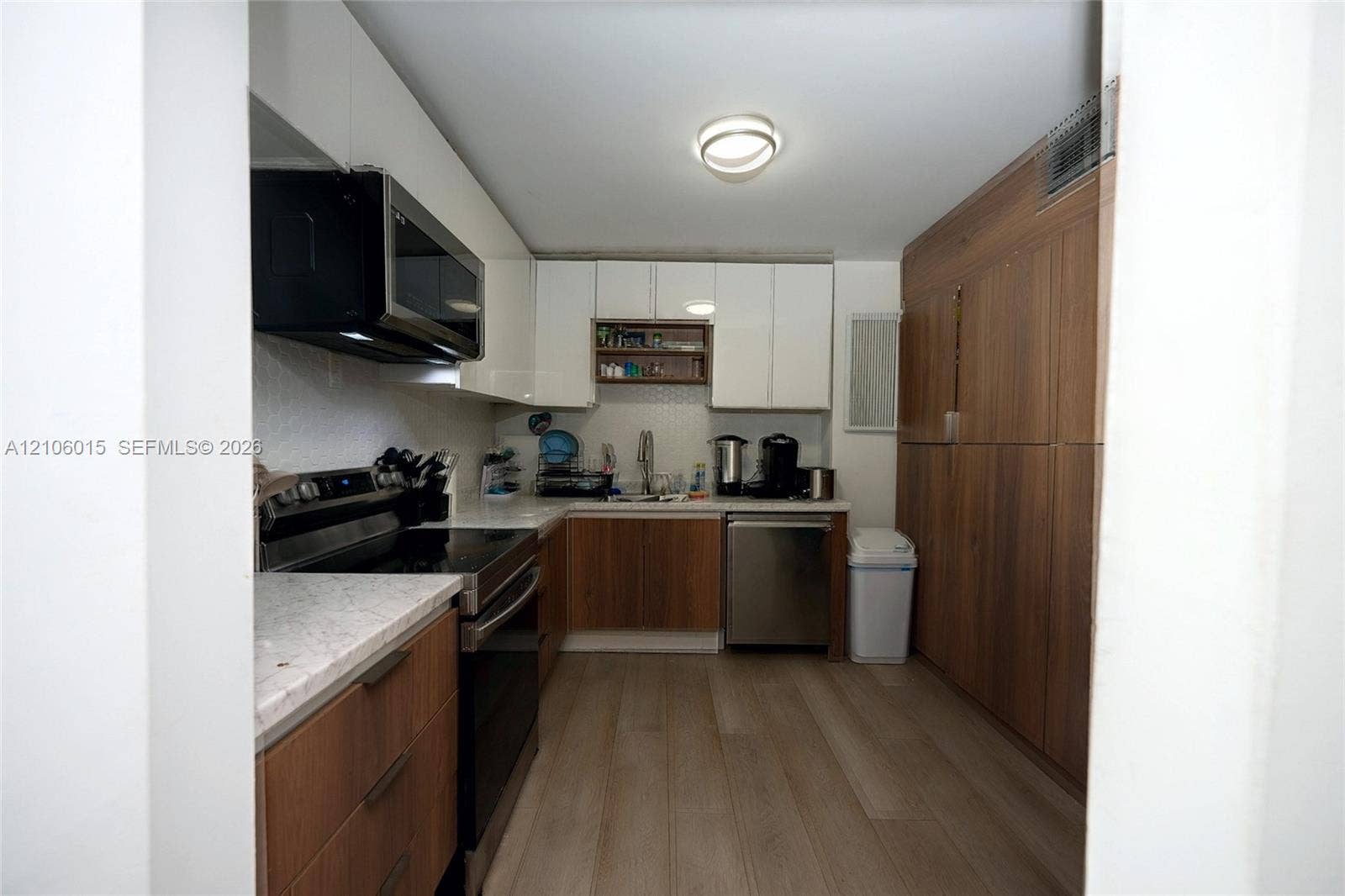 2851 NE 183rd Street, #1109E, Aventura, FL 33160 Kitchen featuring a combination of white upper cabinetry and wood-finish lower cabinetry, stone-finish countertops, stainless steel appliances, and wood-finish flooring