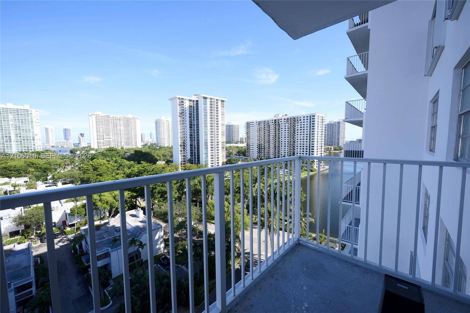 2851 NE 183rd Street, #1109E, Aventura, FL 33160 Private balcony with white metal railings featuring expansive exterior perspectives of the surrounding skyline, dense greenery, and waterway