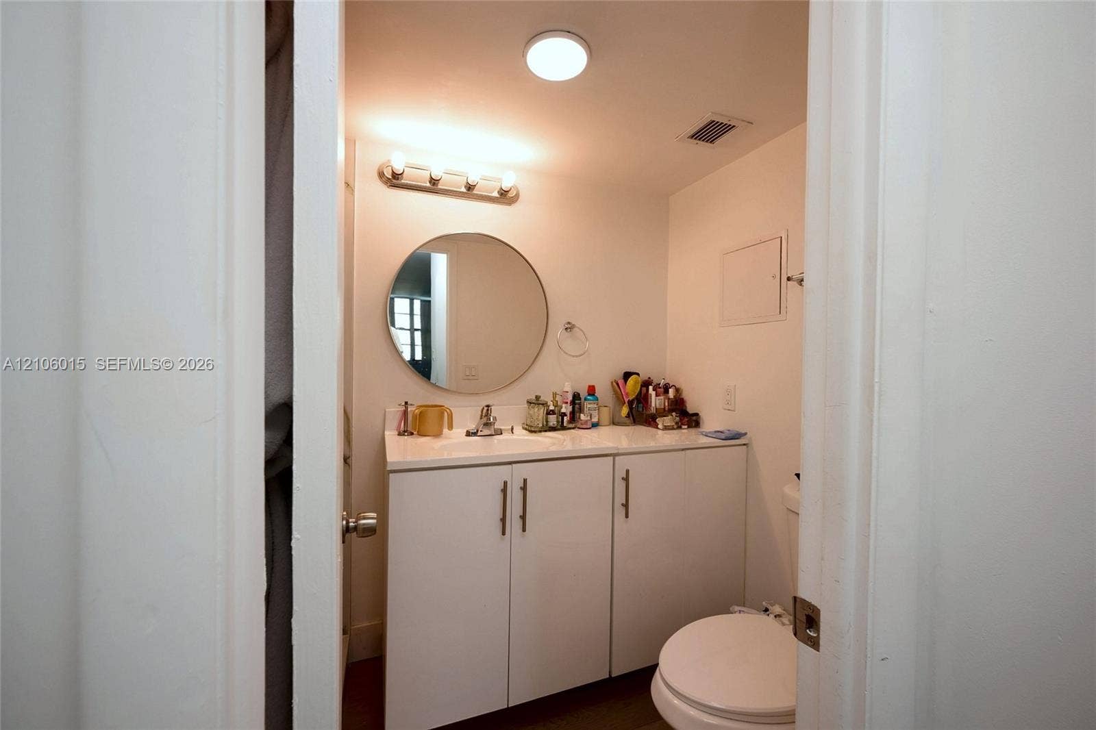 2851 NE 183rd Street, #1109E, Aventura, FL 33160 Bathroom vanity featuring white cabinetry, a solid-surface countertop with an integrated basin, a circular wall-mounted mirror, and a three-light fixture