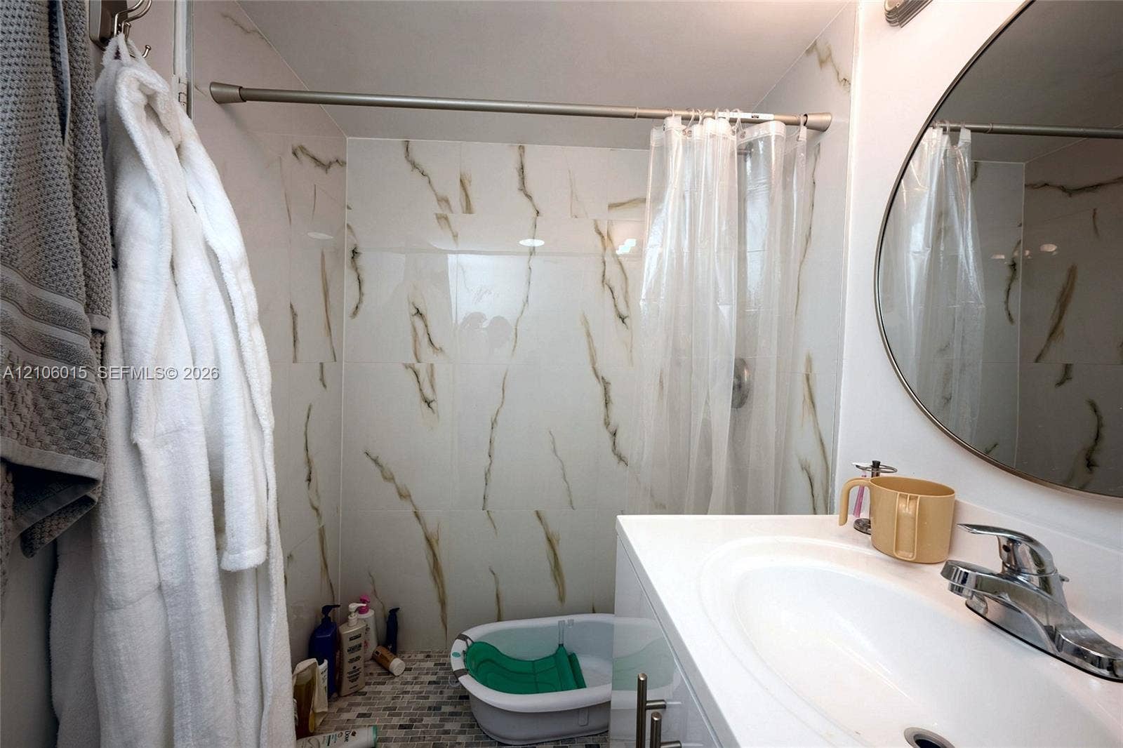 2851 NE 183rd Street, #1109E, Aventura, FL 33160 Full-height shower surround featuring large-format veined tile, vanity with a white integrated basin, polished chrome faucet, and round wall-mounted mirror