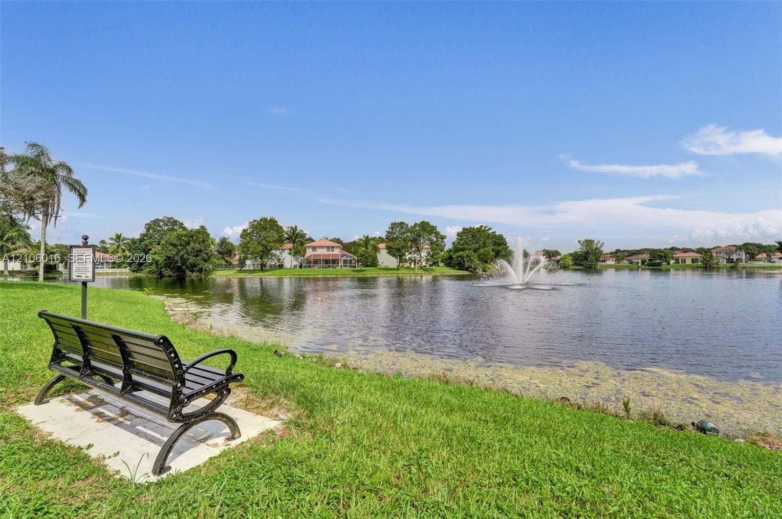 631 NW 135th Terrace, Plantation, FL 33325 Waterfront setting featuring a concrete pad, metal bench, mature landscaping, and a central fountain