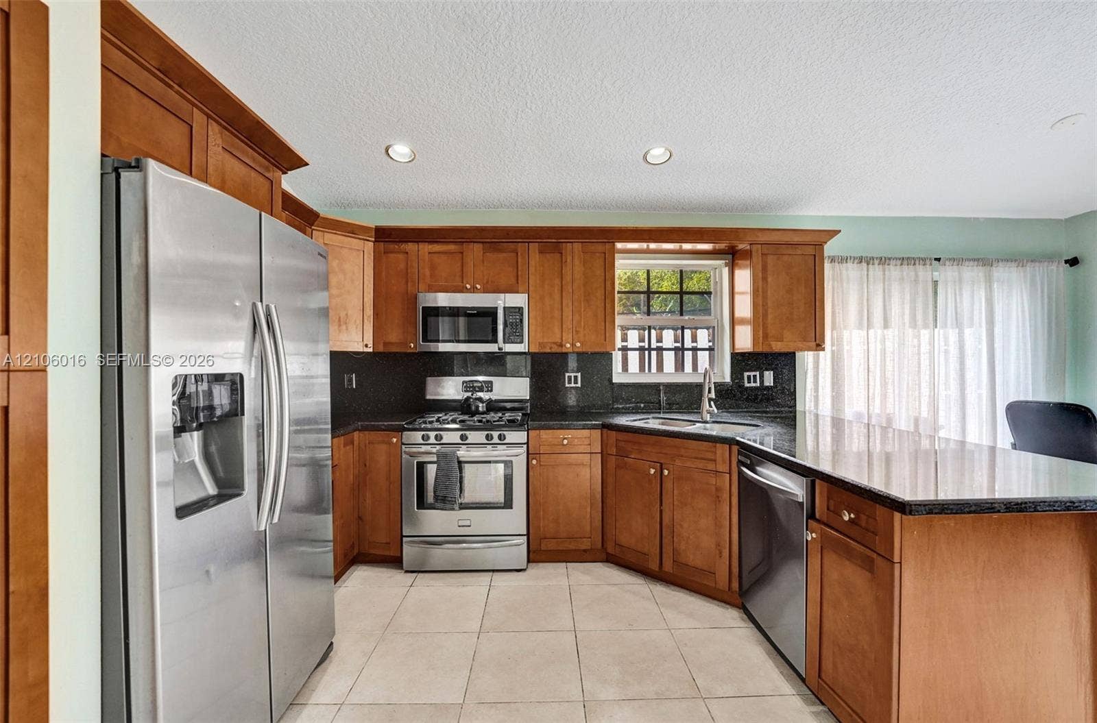 631 NW 135th Terrace, Plantation, FL 33325 Kitchen featuring wood cabinetry, dark stone-finish countertops, stainless steel appliances, a peninsula with an integrated dishwasher, and tile flooring