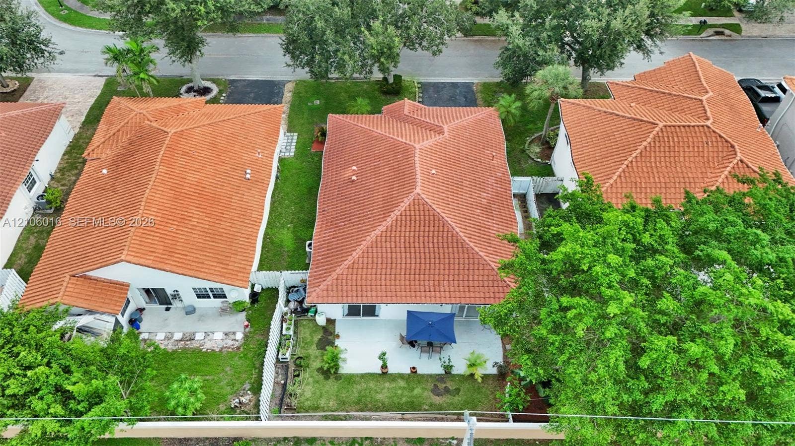 631 NW 135th Terrace, Plantation, FL 33325 Aerial perspective of a residence featuring a terracotta-style tile roof, a paved ground-level patio, and a lawn area enclosed by a white vinyl privacy fence