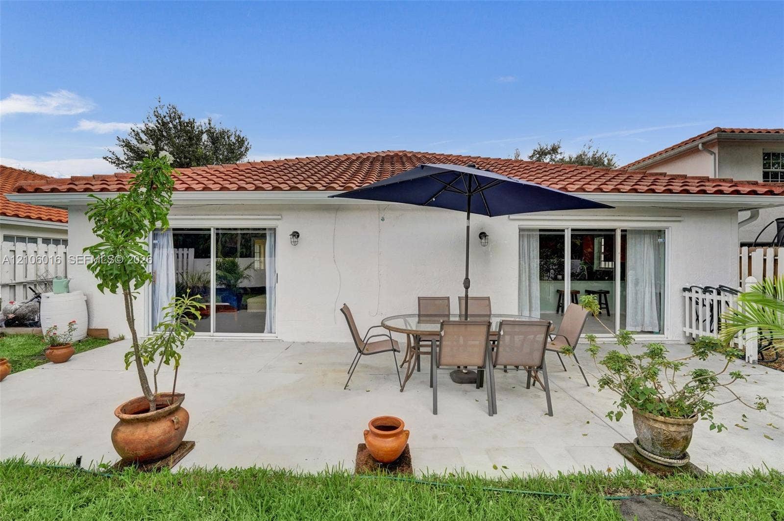 631 NW 135th Terrace, Plantation, FL 33325 Concrete patio area featuring dual sliding glass doors, exterior wall-mounted lighting, and a terracotta tile roof